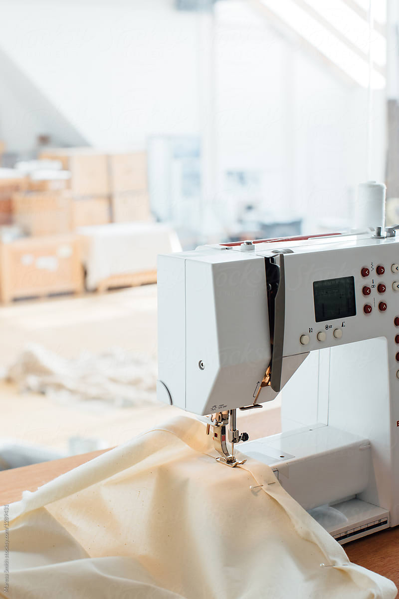 A sewing machine stitching a hem on calico fabric. A white blurry studio space in the background