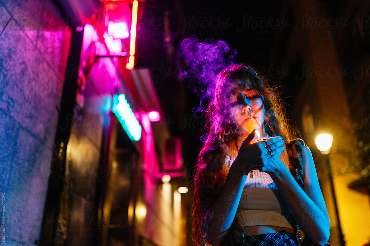 redhead woman lights a cigarette in the street at night