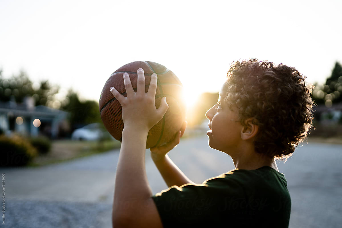 Profile of curly haired boy lining up basketball shot
