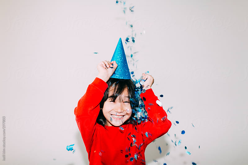 Young mixed race boy in blue party hat plays with confetti by kelli kim ...