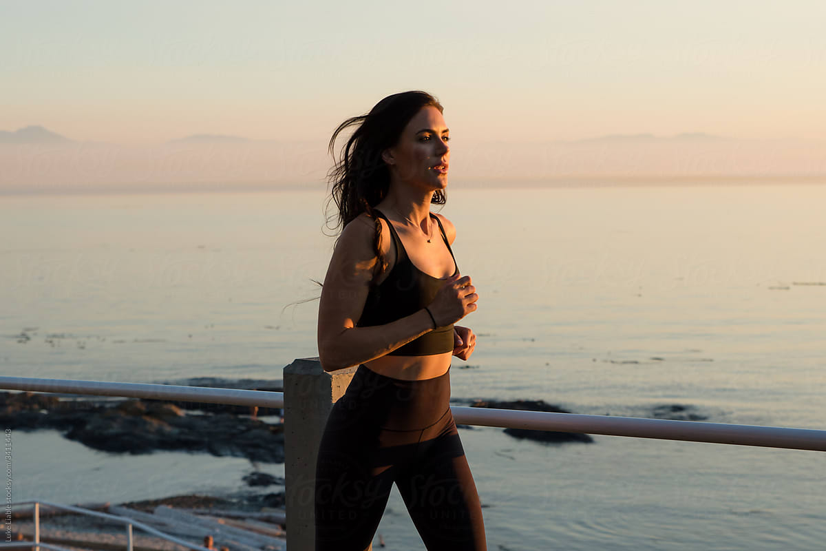 Fit women running at sunset by the ocean.