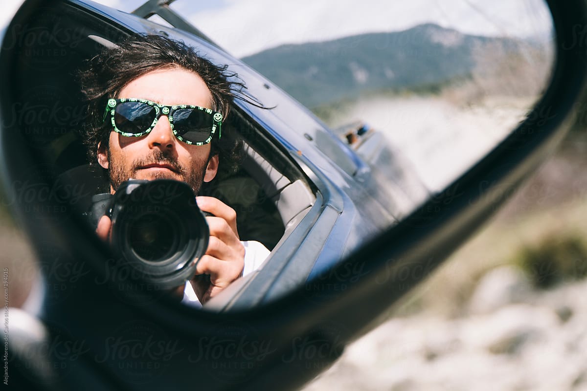 Young man taking a selfie with a dslr on a truck driving mirror