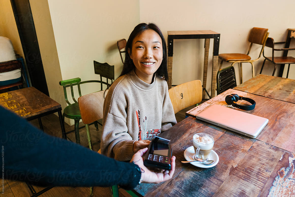 Cheerful Asian woman paying for coffee with credit card