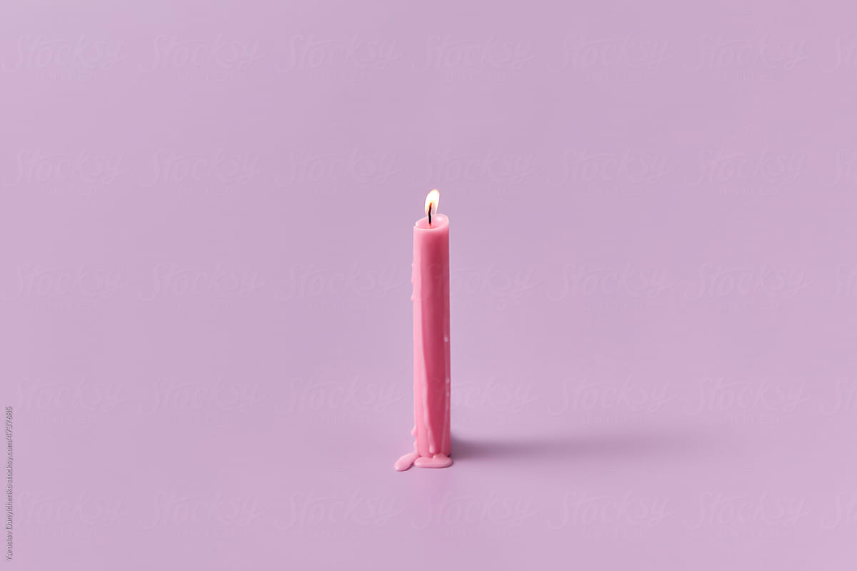 Burning long candle on pink background.