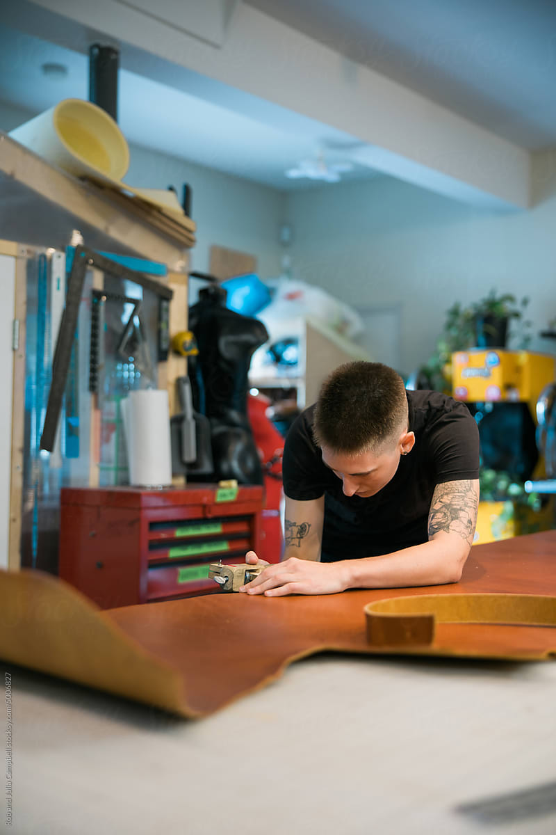 Person cutting leather hide and making a belt.