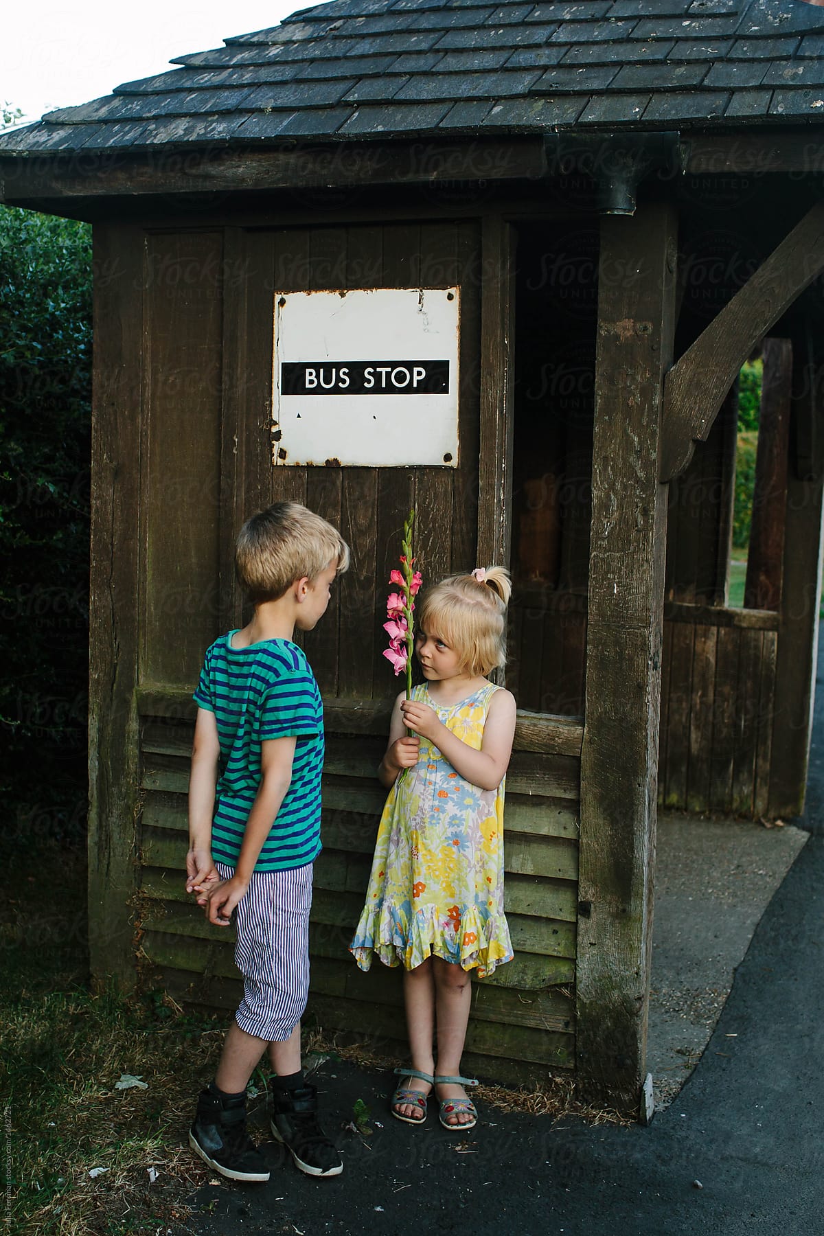 A boy and girl chat to each other while they wait for a bus.