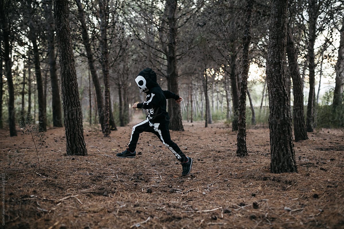 Child in skeleton costume hopping in forest