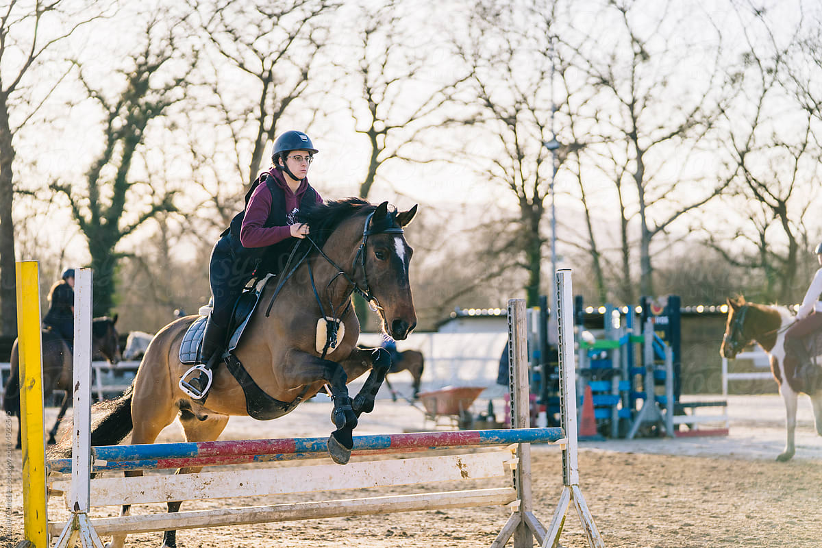 Focused female jockey on horse jumping over barrier