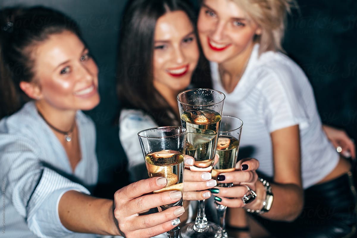 Three pretty young girls friends have fun together drinking champagne on party