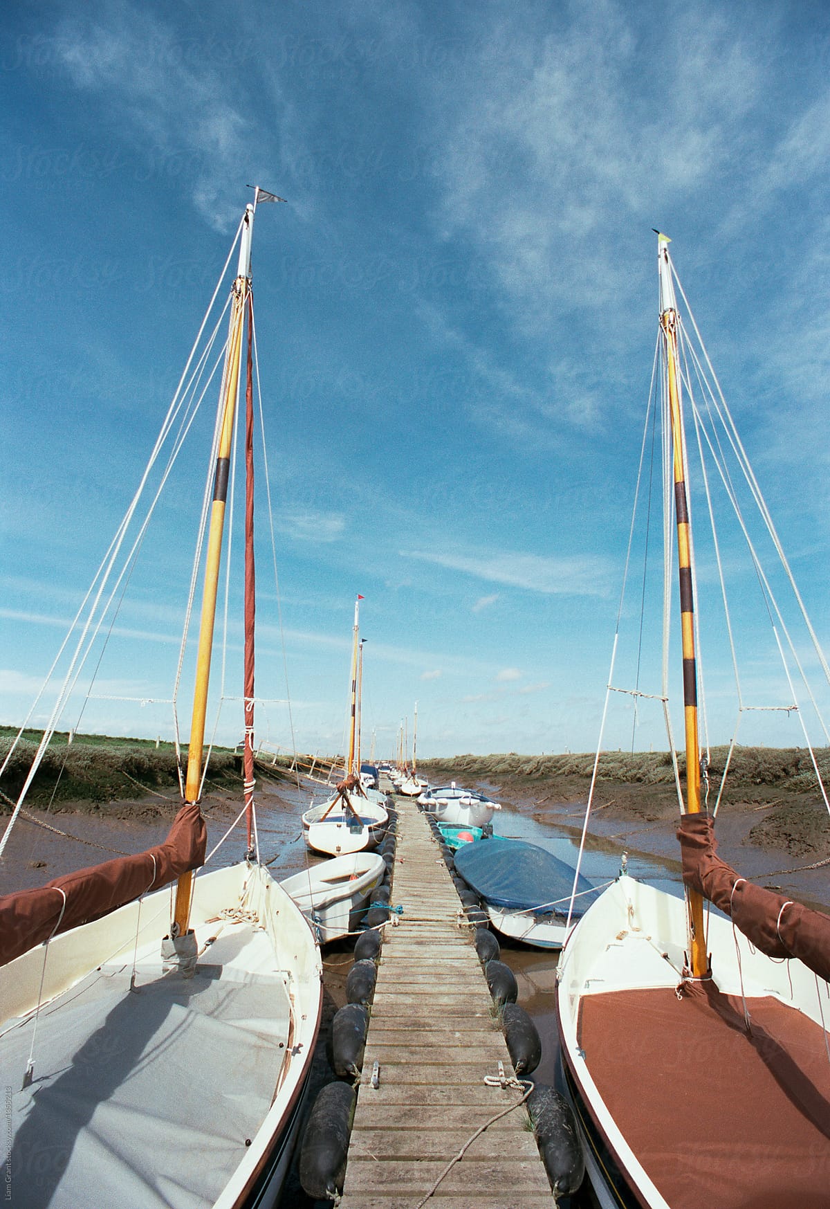 Sailing boats moored beside a jetty at low tide. Morston Quay, N