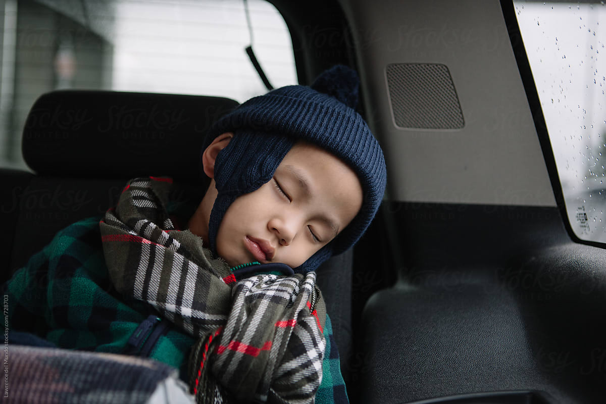 Young child wearing a seatbelt in car booster seat falls asleep during a road trip