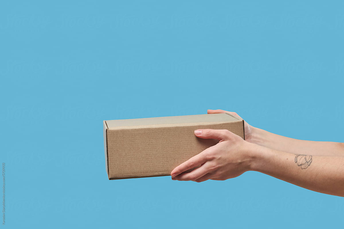 Cardboard box in woman's hands over light blue studio background