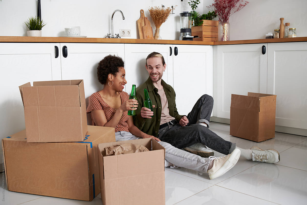 young couple clinking bottles of beer at new apartment