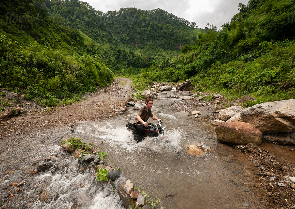 A backpacker crossing a river on a motorbike