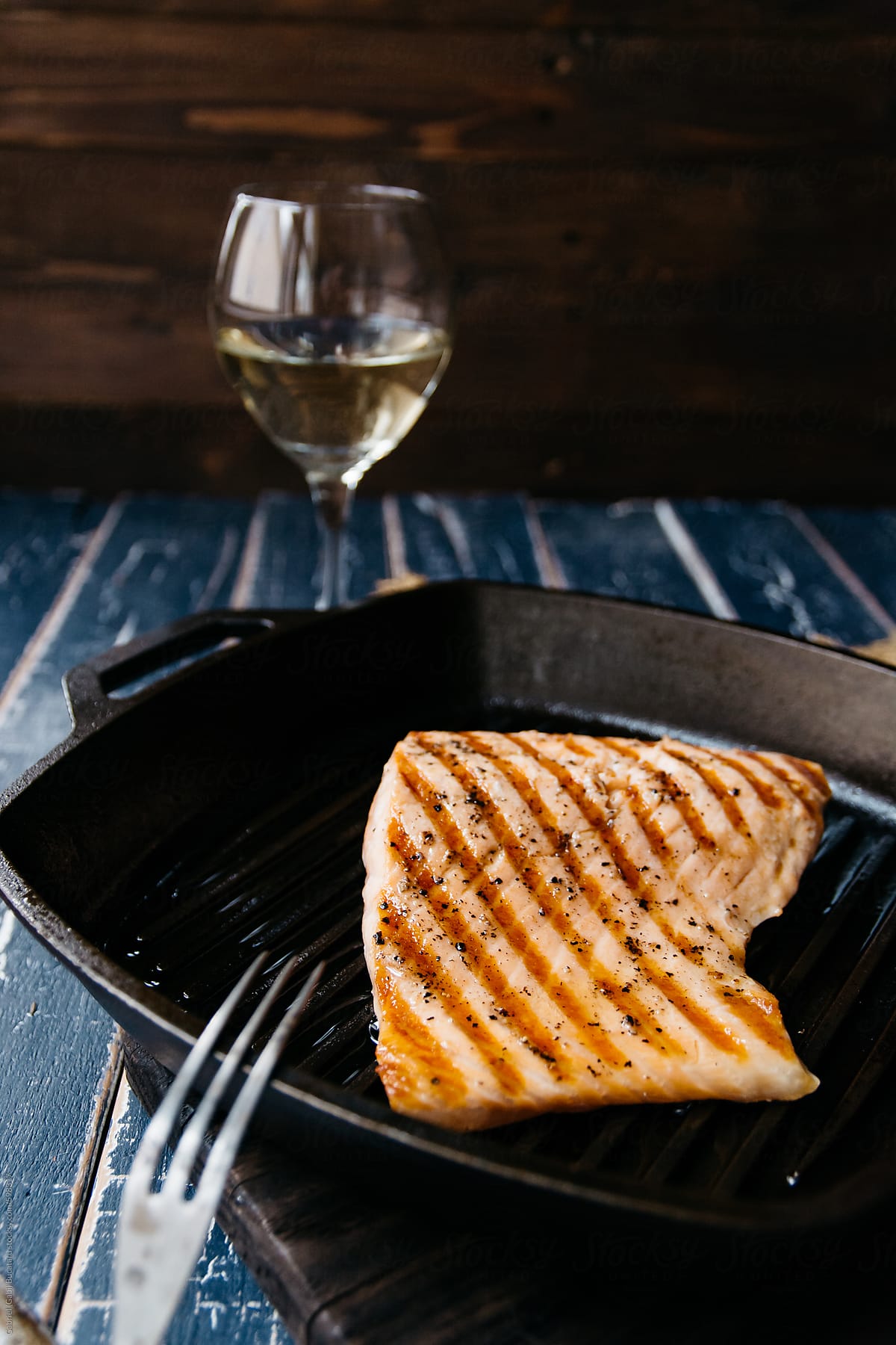 Grilled salmon in a cast iron griddle pan with a glass of white wine