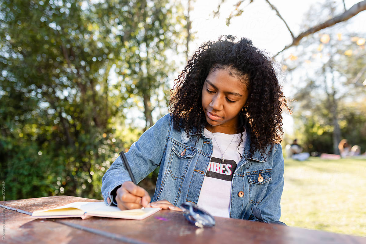 Woman Focuses on Writing While Sitting at a Picnic Table in the Park