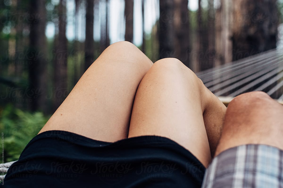 Woman and man\'s knees lounging in a hammock outdoors