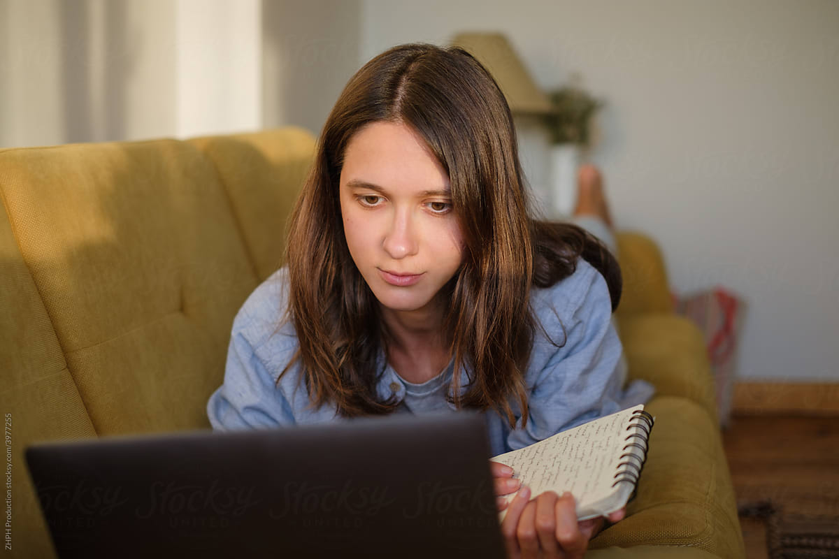 Woman with laptop and notebook lying on the sofa at home