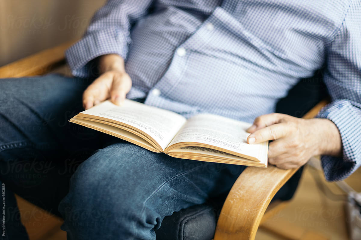 Unrecognizable man reading a book in an armchair
