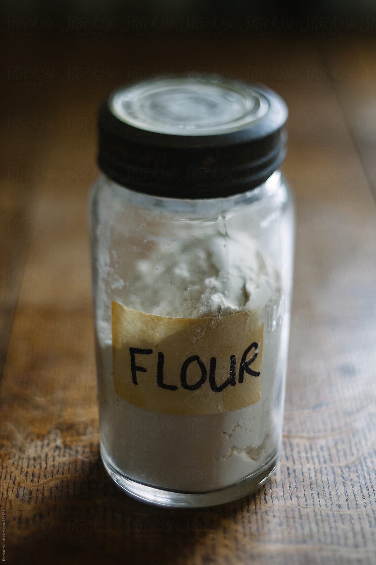 Old glass jar of flour on wooden table.