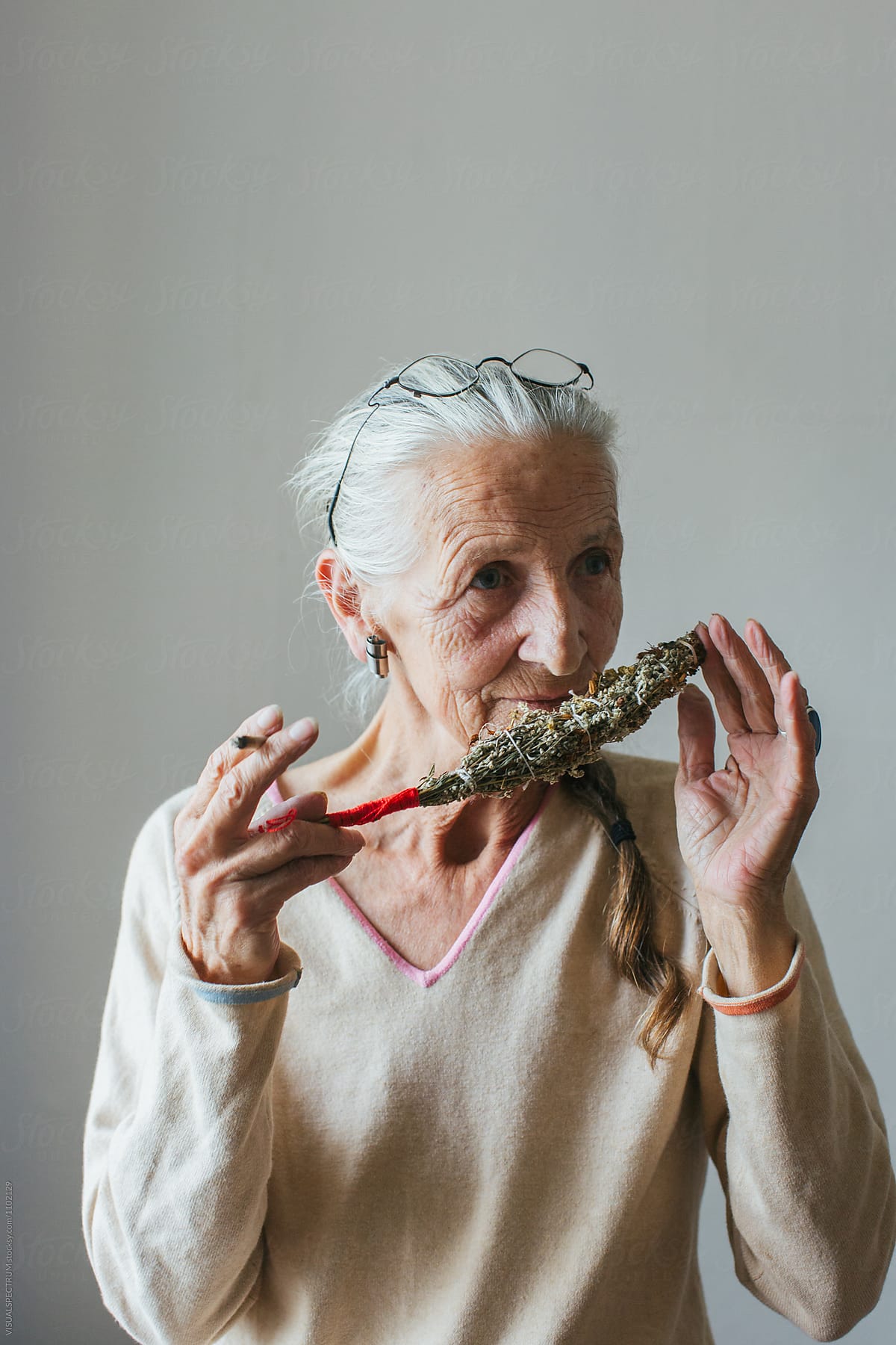 Indoor Portrait of Senior Smoking Woman with Grey Hair Smelling Self-Made Smudge Stick