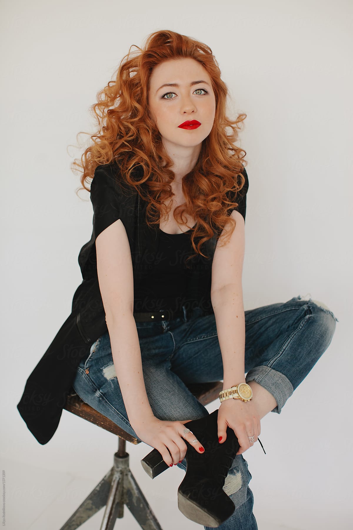 Portrait of young fashionable woman with red curly hair posing at studio