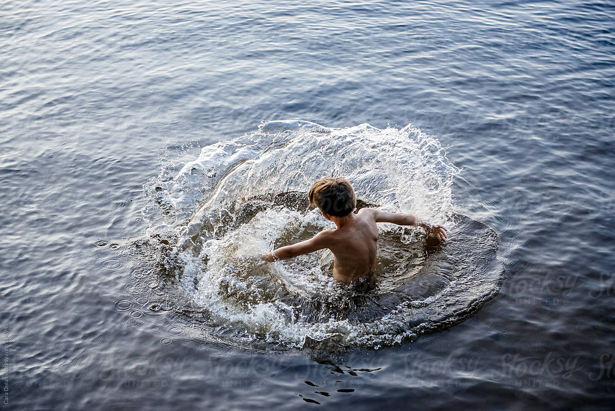 Boy swimming in a lake makes a wave with his hand