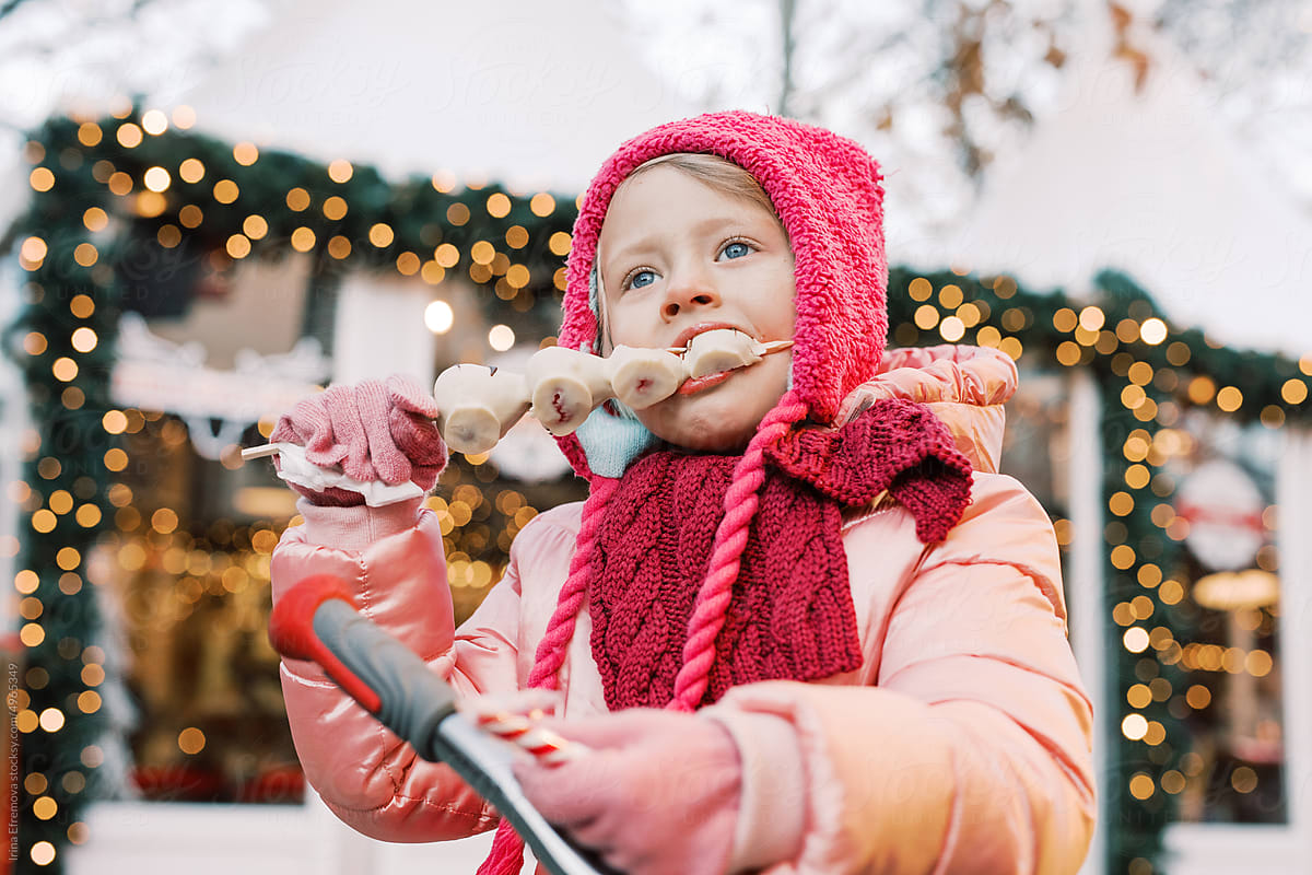 Girl in pink winter clothes eats white chocolate strawberry outside