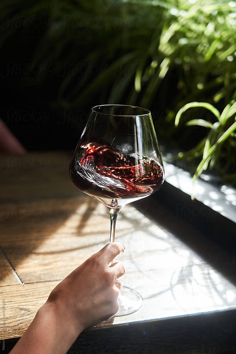Woman\'s hand waving glass of red wine at sunlit table
