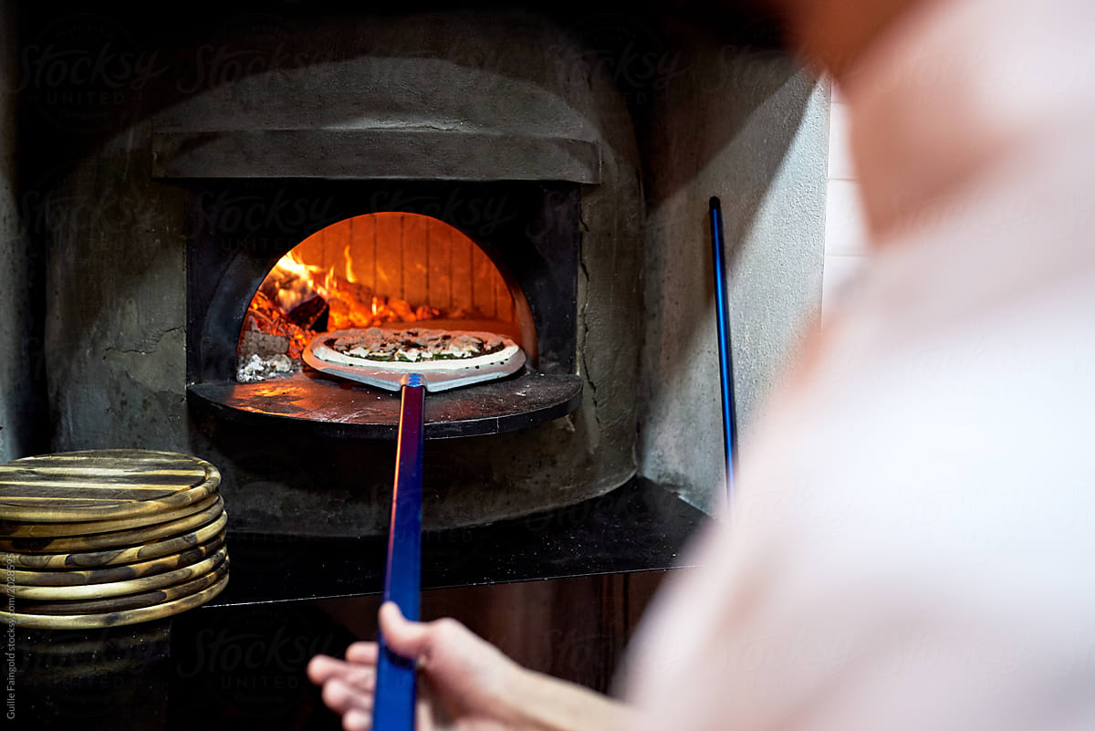 Chef putting pizza into wood fired stove.
