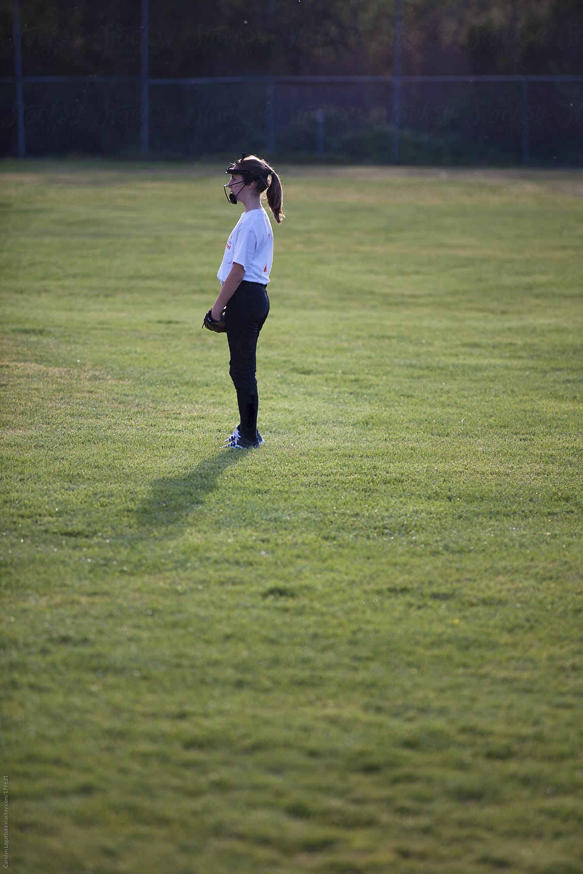 Young girl standing in the outfield at a softball game