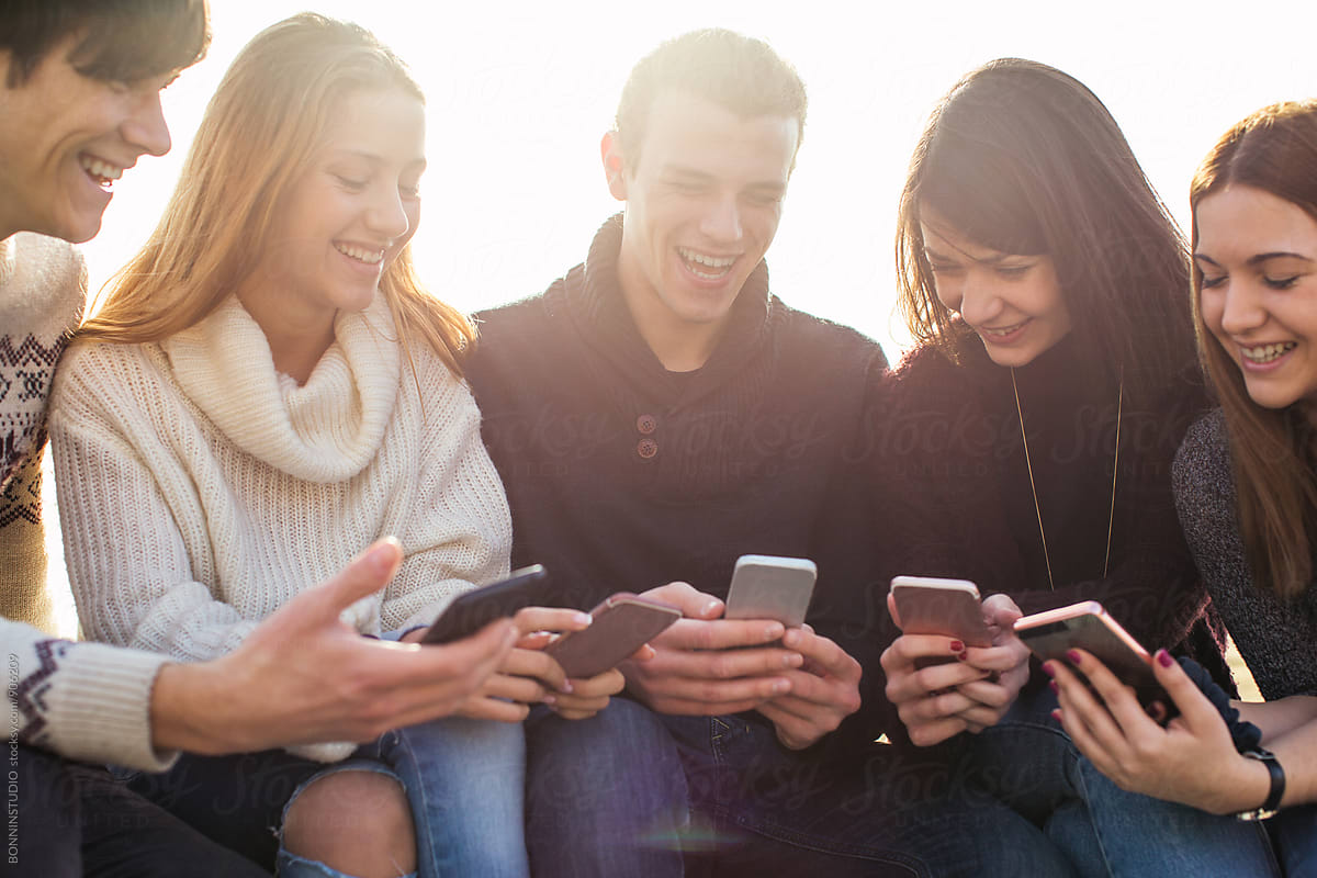 Group Of Happy Teen Friends Using Their Smartphones Outside By