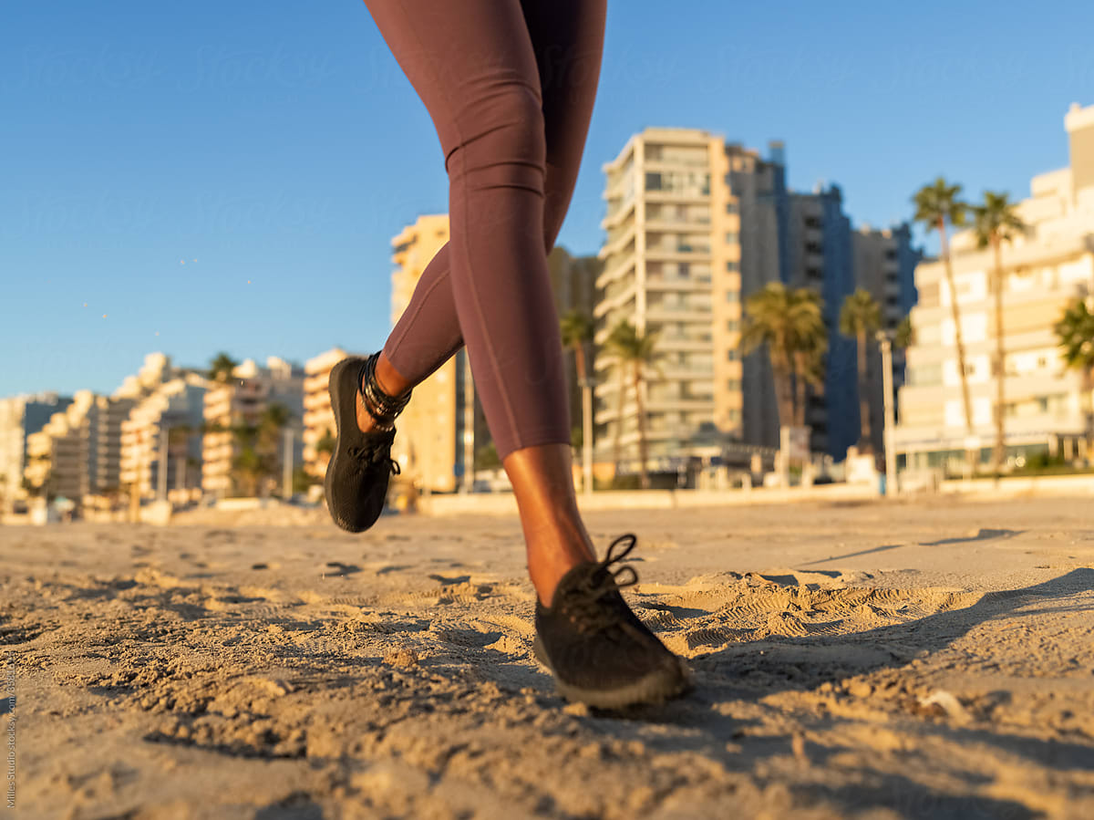 Crop female athlete running on sand
