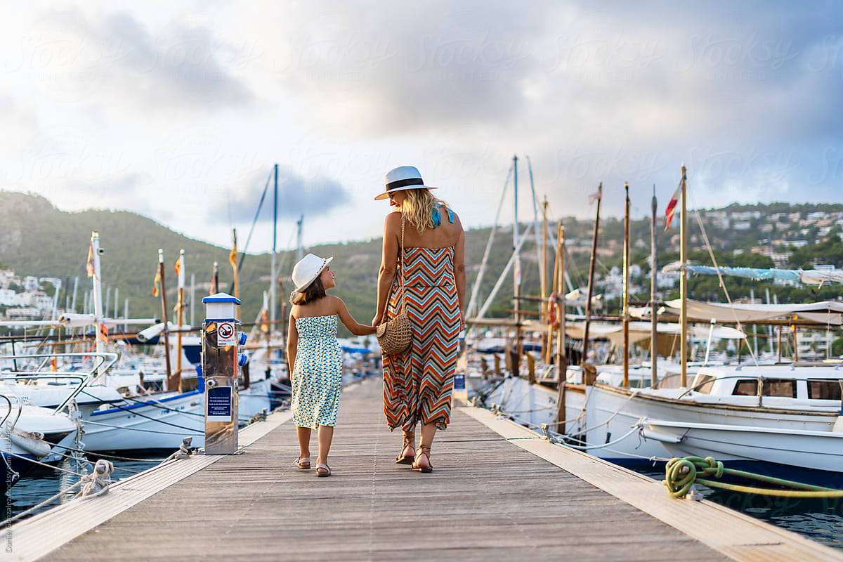 Woman with daughter walking between sailboats
