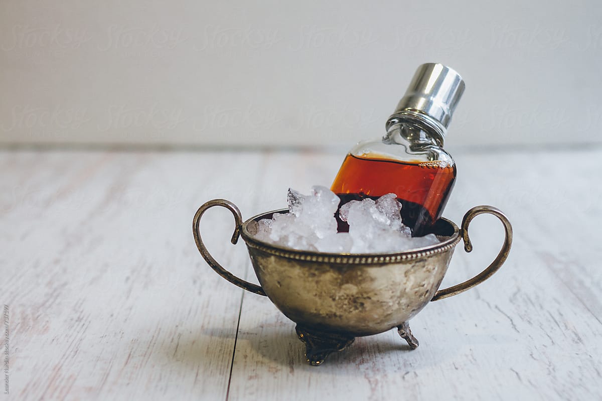 classic manhattan cocktail served in a flask on ice in a silver bowl