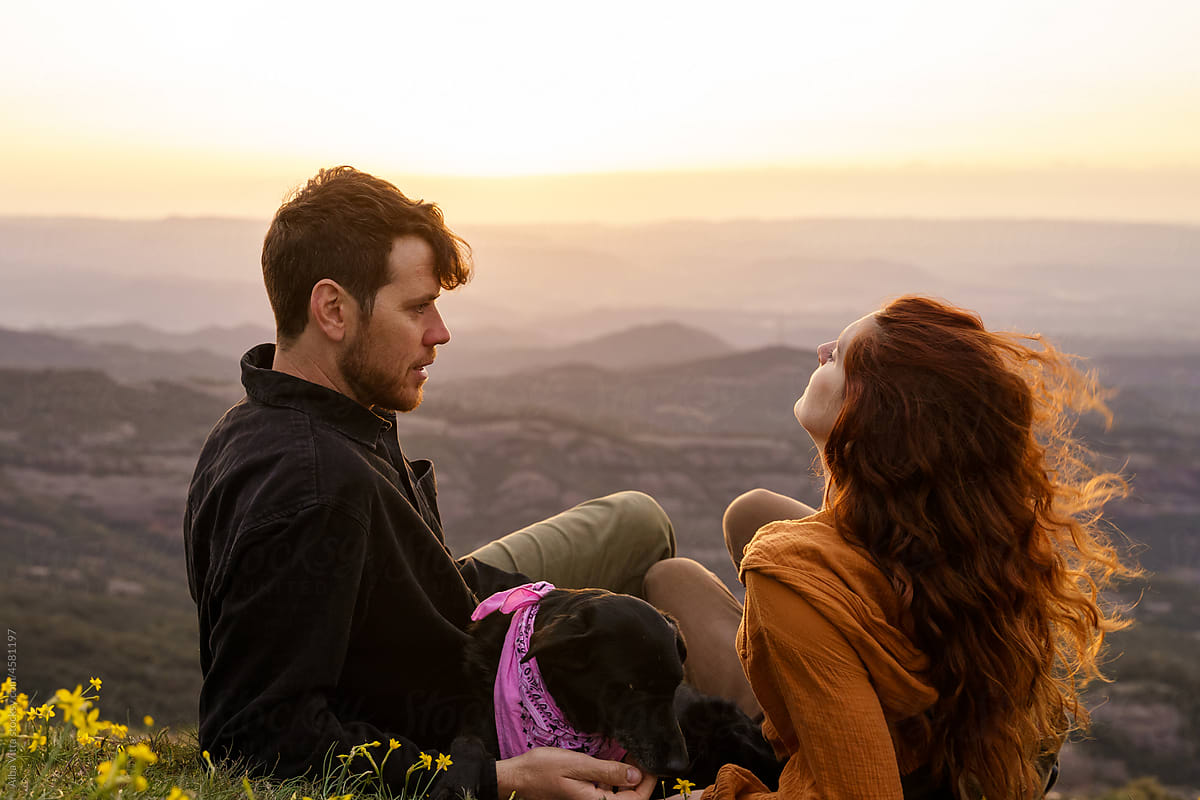 Portrait of young loving couple in the mountain at sunset with dog