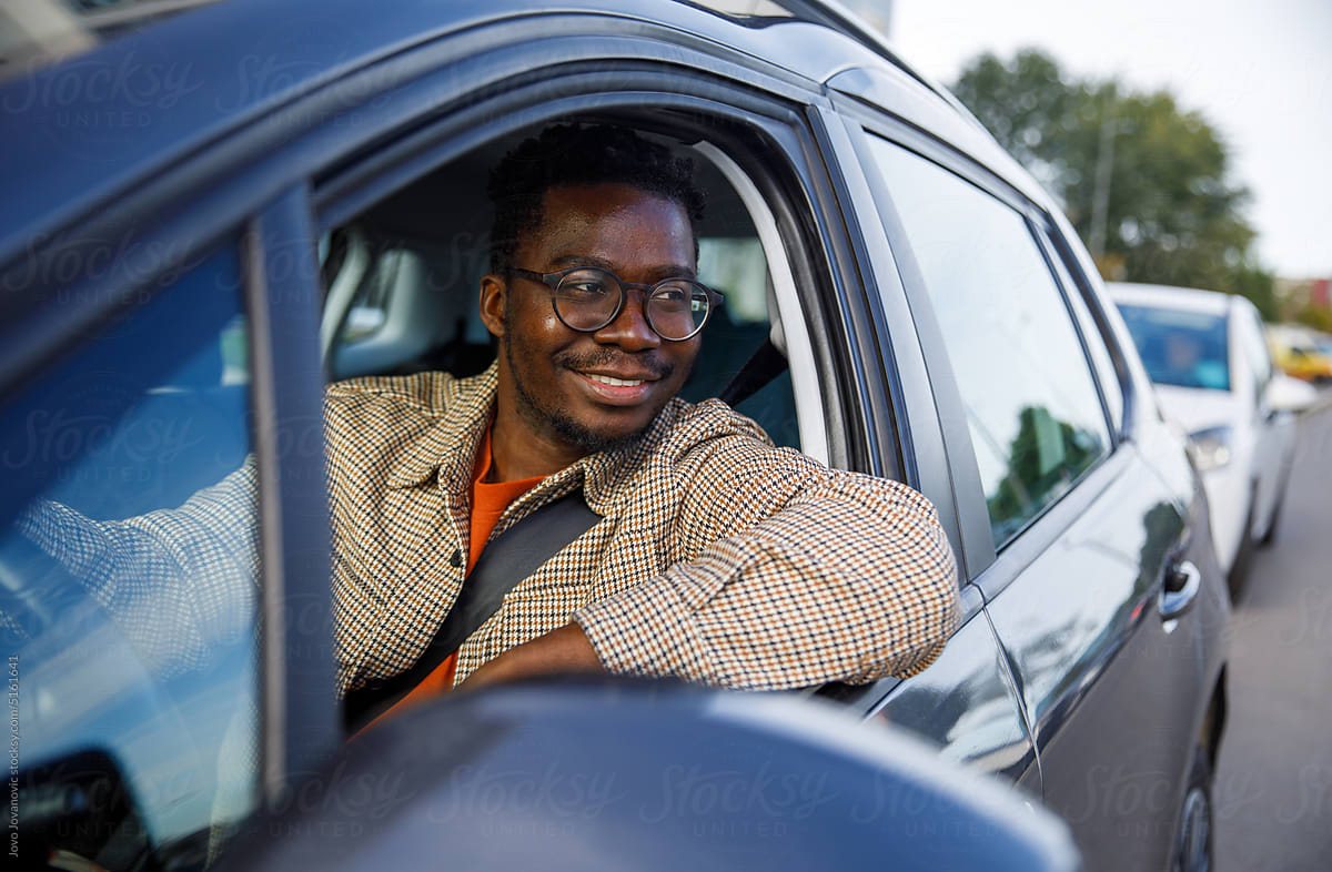 Happy man driving car looking away through open window and smiling