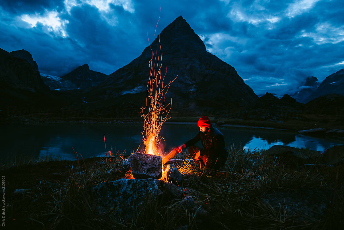 Traveler near bonfire on dark shore of lake