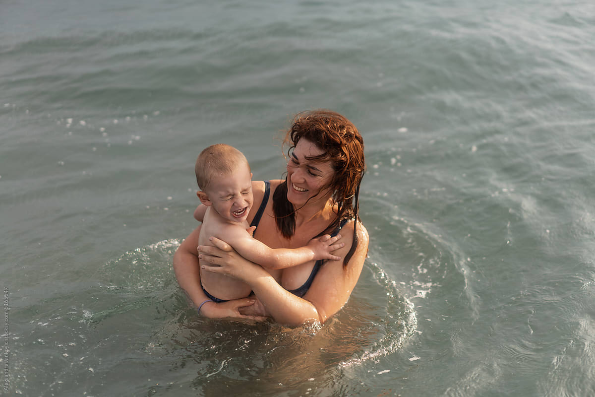 Woman Holding A Crying Child In The Water At The Beach