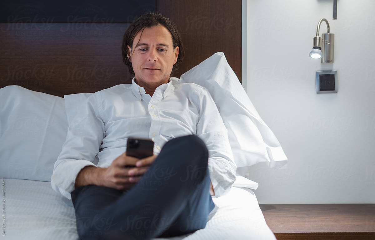 Elegant man browsing smartphone on bed