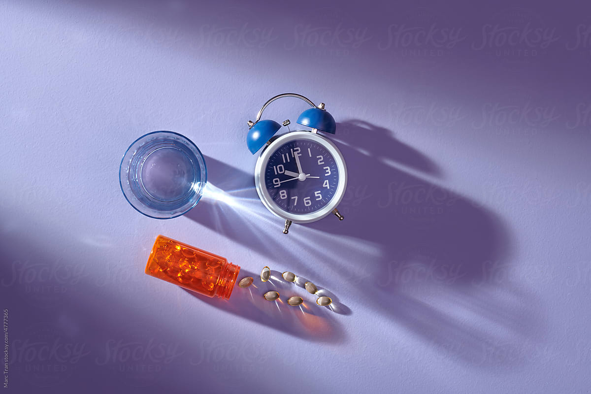 Orange bottle with oil pills, glass water   and alarm clock