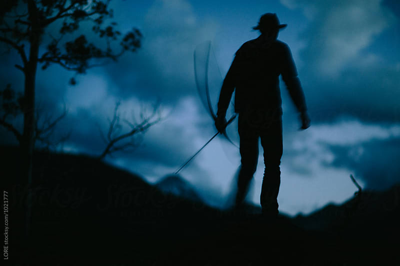 one adult male walks with bow and arrow at dusk in the forest