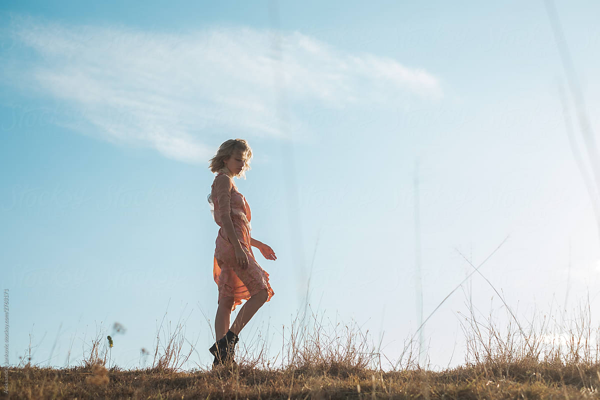 Woman Wearing Sundress Walking In The Grassland Against The Blue Sky