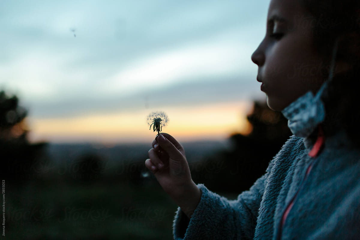kid blowing a dandelion outdoor at twilight