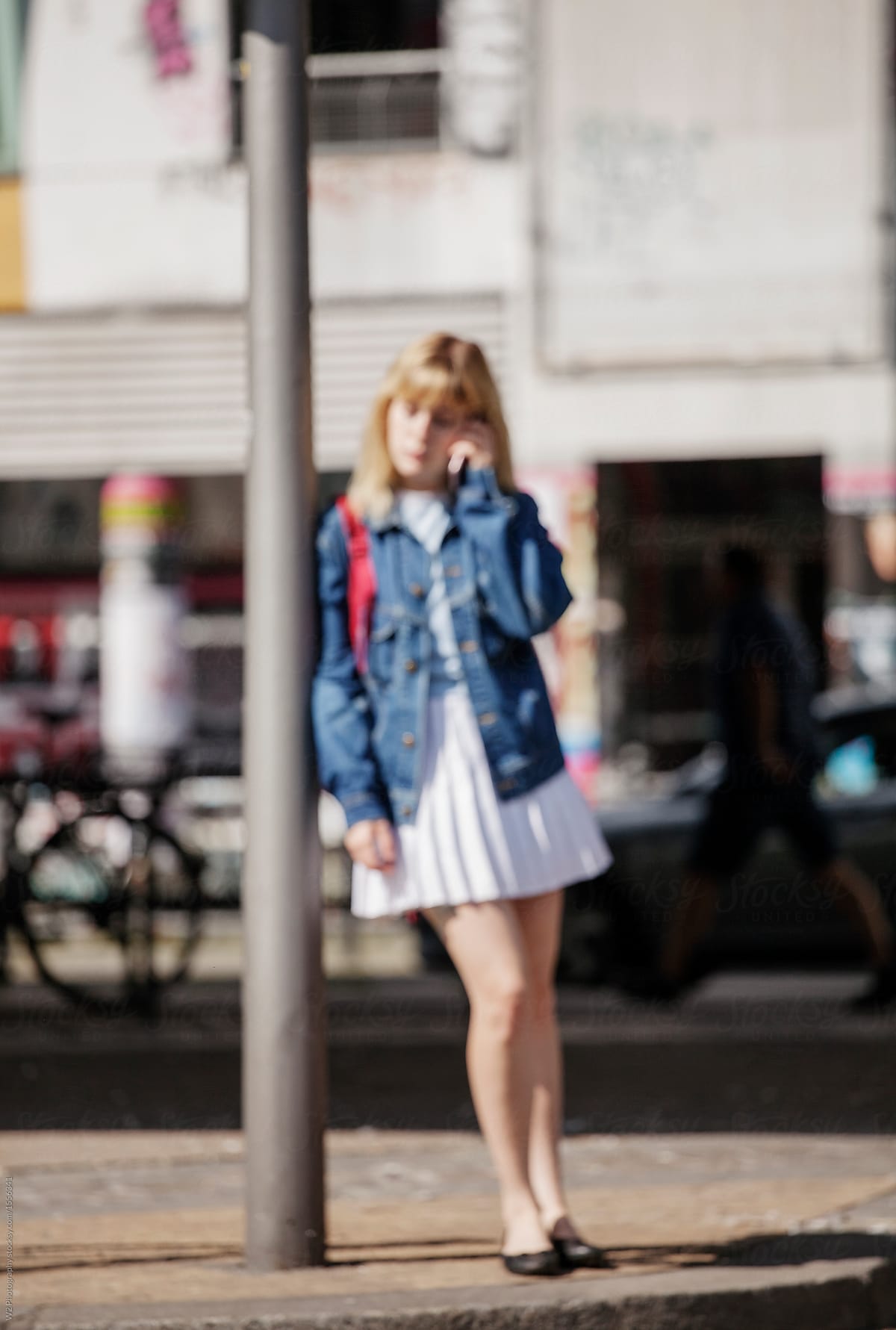 Out of focus image of a woman using her phone and leaning on a lamp post.