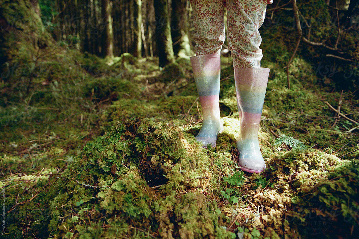 Girl's feet in rainbow rain shoes in the forest