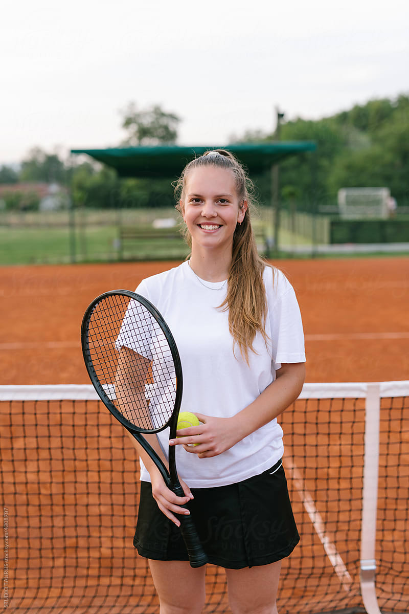 Young happy girl portrait standing on a tennis court