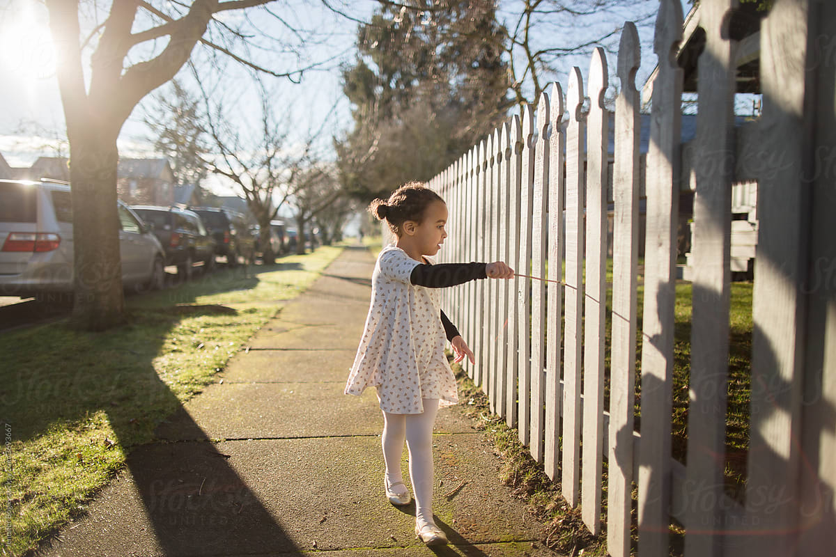 Girl walks along white picket fence