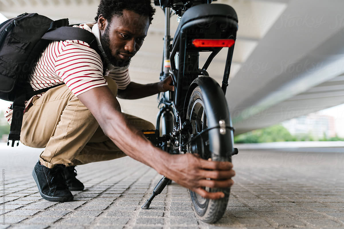 Black guy checking tire of electric bicycle