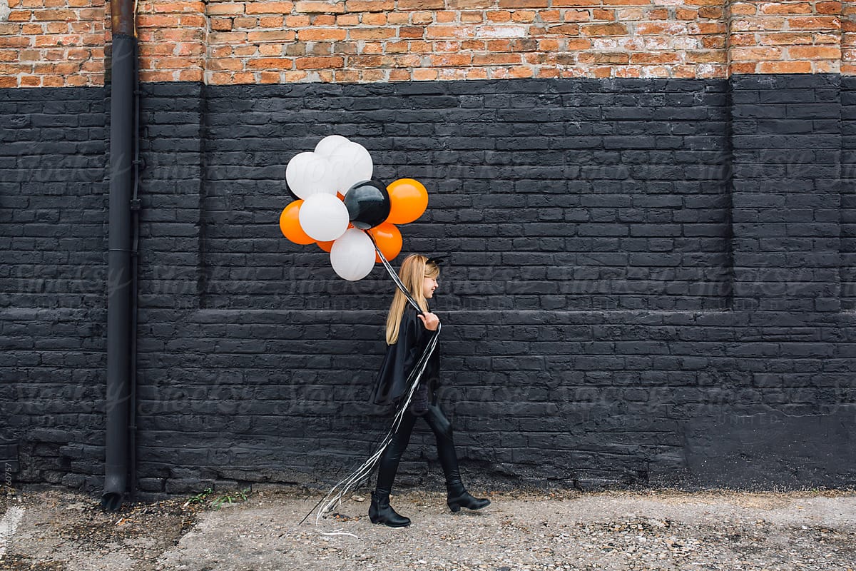 Blonde Girl in a Witch Halloween Costume Holding Balloons
